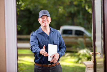 A service man with clipboard greeting with a handshake at a front door.